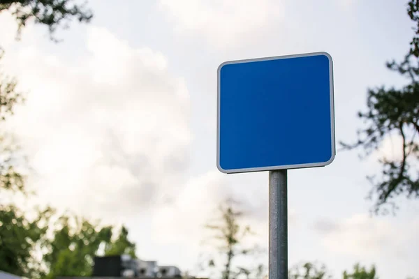 Blå fyrkantig tom vägskylt närbild på suddig bakgrund himmel med moln och träd — Stockfoto