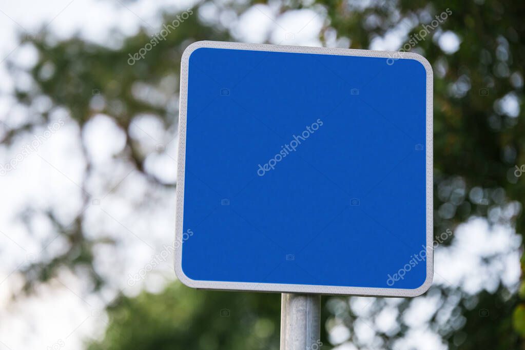 blue square blank road sign closeup on blurred background sky and tree