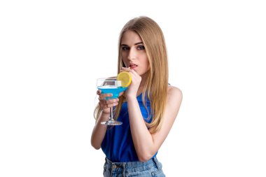 Parlak mavi kotlu ve bluzlu bir kız limonlu mavi bir kokteyl içiyor. Mutlu genç bayan alkolle dinleniyor. Beyaz bir arkaplanda izole edilmiş