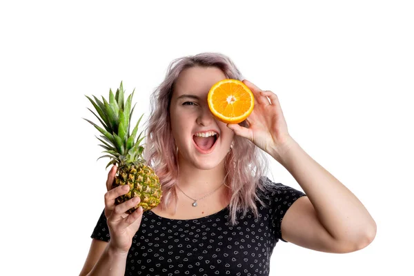 Blond girl with crazy positive emotions in black blouse with a pineapple and orange in her hands. The concept of healthy eating is vegan and vegetarian. Isolated on a white background