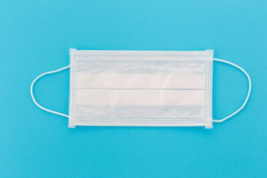 Tek bir tıbbi maskenin üst görüntüsü. Doktorun tek kullanımlık solunum cihazı. Mavi bir arkaplanda izole edilmiş