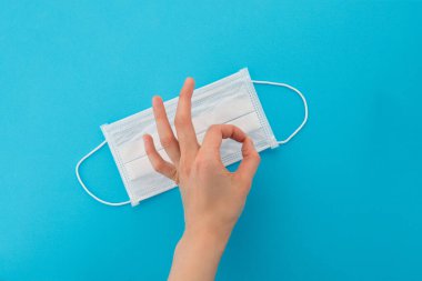 Tek bir tıbbi maskenin üst görüntüsü. Doktor iyi hareket ediyor ve tek kullanımlık solunum cihazı takmayı onaylıyor. Mavi bir arkaplanda izole edilmiş