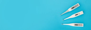 Üç termometrenin üst görüntüsü. İnsan vücudunun sıcaklığını ölçmek için elektronik cihaz. Mavi arkaplanda izole edilmiş, metin için alanı kopyala