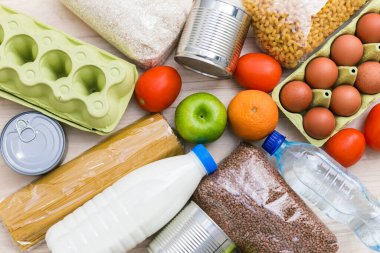 Yağ, süt ve su, otlar, elmalar ve portakallar, tahıllar ve konserve yiyecekler, pirinç ve makarna. İskandinav iç mimarisinde ahşap mutfak masası. Flatlay, üst görünüm