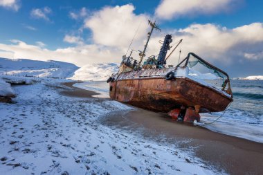Yan yatmış bir balıkçı teknesi, Barents Denizi kıyısında bir fırtınayla karaya vurmuş, Kola Yarımadası, Teriberka, Rusya
