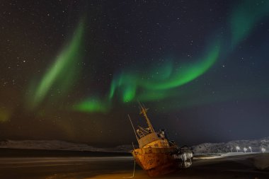 Yıldızlı gökyüzünde kutup ışıkları. Kenarda yatan bir balıkçı teknesi, Barents Nehri 'nin kıyısında bir fırtınayla karaya vurmuş. Teriberka, Rusya