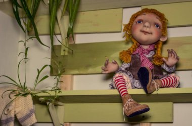 Yumuşak tekstil el yapımı oyuncak kız rafta benekli bir elbiseyle oturuyor.