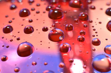 Bir bardağa iliştirilmiş parlak berrak su noktası, camdaki renkle aynı rengi yansıtır. Dekorasyondaki gibi güzel bir arka plana.