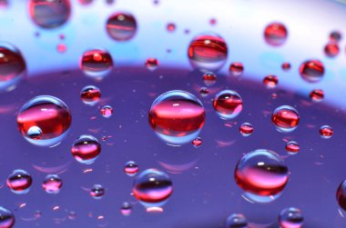 Bir bardağa iliştirilmiş parlak berrak su noktası, camdaki renkle aynı rengi yansıtır. Dekorasyondaki gibi güzel bir arka plana.