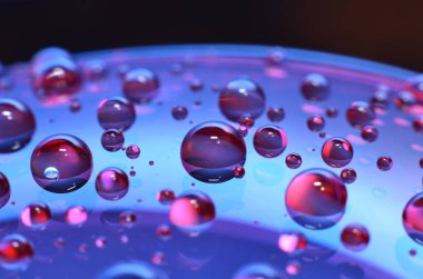 Bir bardağa iliştirilmiş parlak berrak su noktası, camdaki renkle aynı rengi yansıtır. Dekorasyondaki gibi güzel bir arka plana.