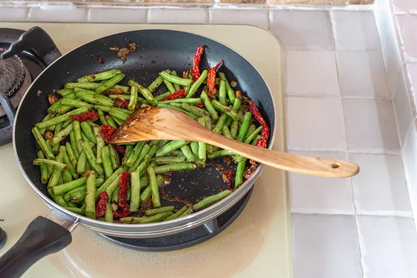 Comida caseira. Feijão verde francês, pimentão seco e alho em frigideira no fogão de cozinha — Fotografia de Stock