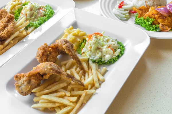 İki parça kızarmış tavuk kanadı, patates kızartması, peynirli makarna ve yeşil marullu taze lahana salatası.