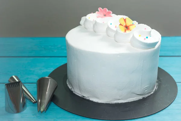 Fresh cream white frosted cake and box of piping nozzles on blue rustic table — ストック写真