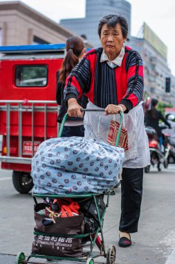 Yaşlı bayan eşyalarla dolu arabayı işlek yoldan geçiriyor..