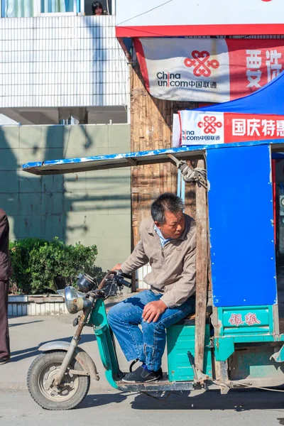 Elektrikli trişördeki Asyalı Çinli bir adam, başı arkaya dönük trafiğe bakıyor.