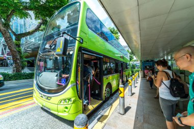 Otobüs durağında bekleyen yolcuların geniş açılı görüntüsü. Singapur yeşil çift katlı otobüs durakları yolcuların iniş ve çıkışları için.