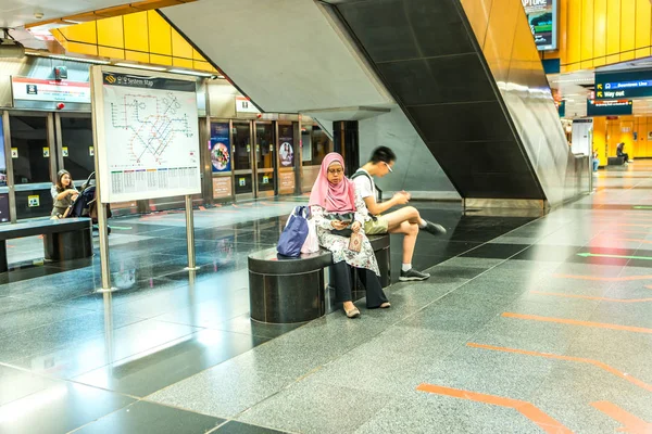 Одна мусульманка в хиджабе, один азиат-подросток, сидящий на скамейке в метро в ожидании поезда, используя мобильный телефон для серфинга в Интернете . — стоковое фото