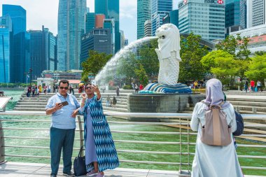 Merlion 'un önünde fotoğraf çeken uluslararası turistler, bir balıkla bir aslanın sembolünü birleştiriyor, gözden kaçırılmaz bir Singapur ikonu..