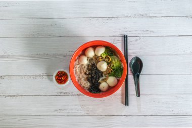 Asya Singapur eriştesi, balık köftesi vermicelli çorbası, kıyılmış kırmızı biberli domuz eti, yeşil sebze ve taze kızarmış ikan billis balığı. Düz üst görünüm.