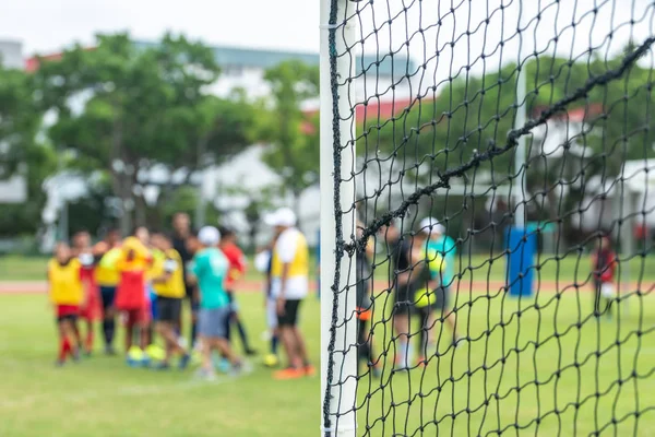 Selective focus side view of soccer goal post net. Football players in blurred bokeh background. — Stock Photo, Image