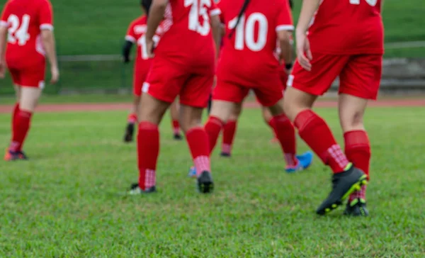 Боке размыла фон неопознанных женщин-футболистов в красной спортивной форме на поле, играющих в футбол — стоковое фото