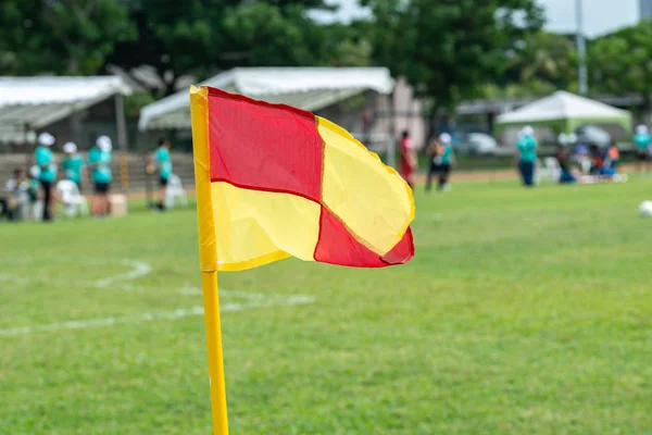 Soccer field corner flag in foreground. Background blurred with unrecognisable football players. Sports and people theme. — Stock Photo, Image