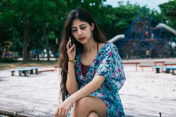 Çiçekli elbiseli uzun saçlı bir Hintli kadın cep telefonuyla konuşuyor..