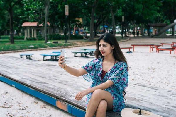 Uma fêmea asiática em vestido floral segurando telefone celular em um parque ao ar livre . Fotografia De Stock