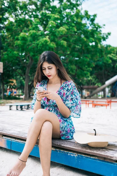 Um cabelo comprido indiano feminino segurando, e digitando no telefone celular com os dedos no parque ao ar livre Fotografias De Stock Royalty-Free
