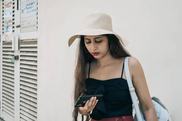 Одна азиатская индийская туристка в шляпе держит и использует мобильный телефон с правой рукой Лицензионные Стоковые Фото