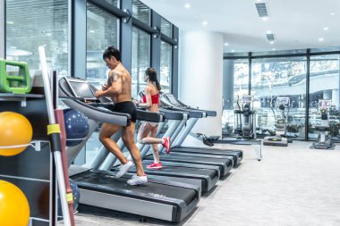 İki yetişkin, üstsüz, kaslı, Asyalı Çinli adam Asyalı bir kadınla koşu bandında koşuyor. Kişisel antrenör, çift aktif egzersiz.