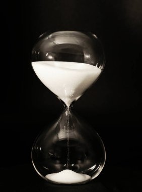 Isolierte Sanduhr mit rinnendem Sand vor dunklem Hintergrund, saat camı