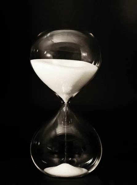 Isolierte Sanduhr mit rinnendem Sand vor dunklem Hintergrund, saat camı