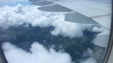 Açık mavi gökyüzünde, beyaz kabarık bulutların üzerinde uçan uçak kanadındaki uçak penceresinden resim gibi hava manzarası.