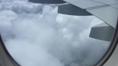 Açık mavi gökyüzünde, beyaz kabarık bulutların üzerinde uçan uçak kanadındaki uçak penceresinden muhteşem bir hava manzarası.