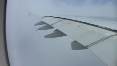 Açık mavi gökyüzünde, beyaz kabarık bulutların üzerinde uçan uçak kanadındaki uçak penceresinden muhteşem bir hava manzarası.