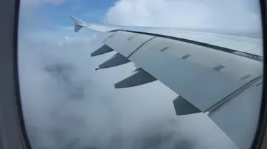 Açık mavi gökyüzünde, beyaz kabarık bulutların üzerinde uçan uçak kanadındaki uçak penceresinden çarpıcı bir hava manzarası.