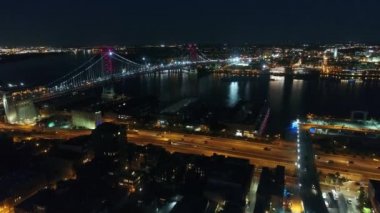Şehir merkezinde, nehrin karşısındaki büyük modern Philadelphia şehrinde gece ışığı altında çarpıcı 4K hava manzaralı bir köprü.