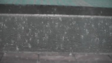 Resimli alçak açı yağmur damlalarının yavaş çekim görüntüsünü tatmin ediyor. Gri, ıslak asfalt kaldırıma sakince düşüyor.