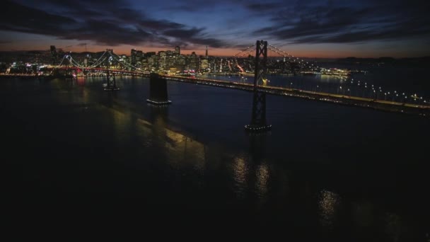 大きな鋼の魅力的な空中ショットゴールデンゲートブリッジサンフランシスコのダウンタウンのスカイラインがライトアップされた夜の街並 — ストック動画