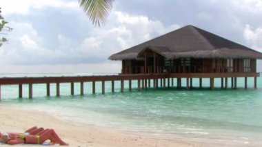 Beyaz tropikal okyanus kumsalında güneşlenen turistlerle dolu büyük, ahşap, lüks bir tatil köyü, bungalov otel dairesi.