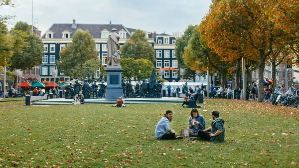Молодежь отдыхает на траве за статуей Рембрандта в Амстердаме. Сентябрь 2017 — стоковое фото
