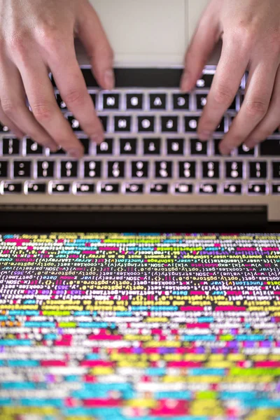 Hands typing on computer keyboard with source code on the screen — Stock Photo, Image