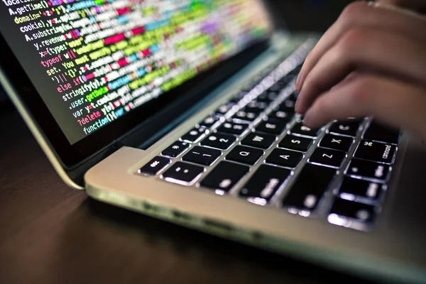 Hands typing on computer keyboard with source code on the screen — Stock Photo, Image