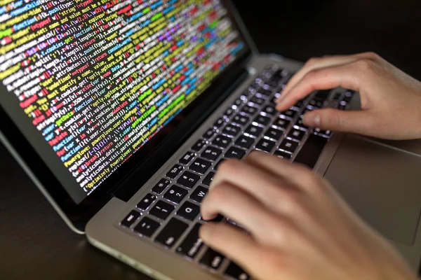 Hands typing on computer keyboard with source code on the screen — Stock Photo, Image