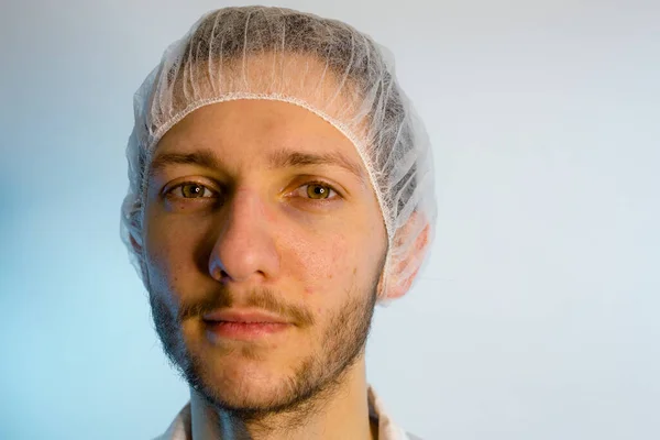 An adult male dressed in a white lab coat with a hair net on. Ready to work in a clean room or laboratory