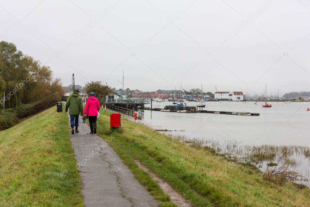 A couple walking their dog along a river path on a dull and rainy day