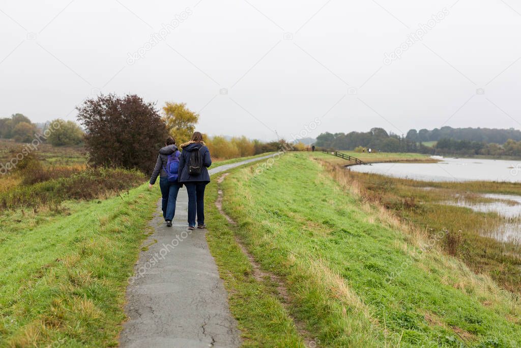2 female friends enjoying a walk along a river path on a dull and rainy autumn day