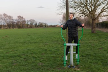 Genç yetişkin bir erkek, parkında bedava spor yapmak için halka açık egzersiz ekipmanları kullanıyor.