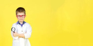 Gözlüklü çocuk, tıbbi önlük ve sarı arka planda mikroskop. Küçük bilim adamları keşifler yapar, deneyler yapar. Bir tedavi, virüs için bir aşı arıyorum. Gelecek konsepti